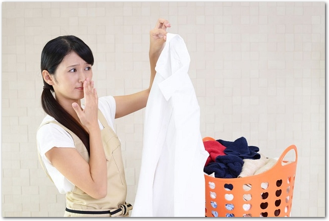 洗濯物の白シャツをつまんで鼻を押さえる主婦の様子